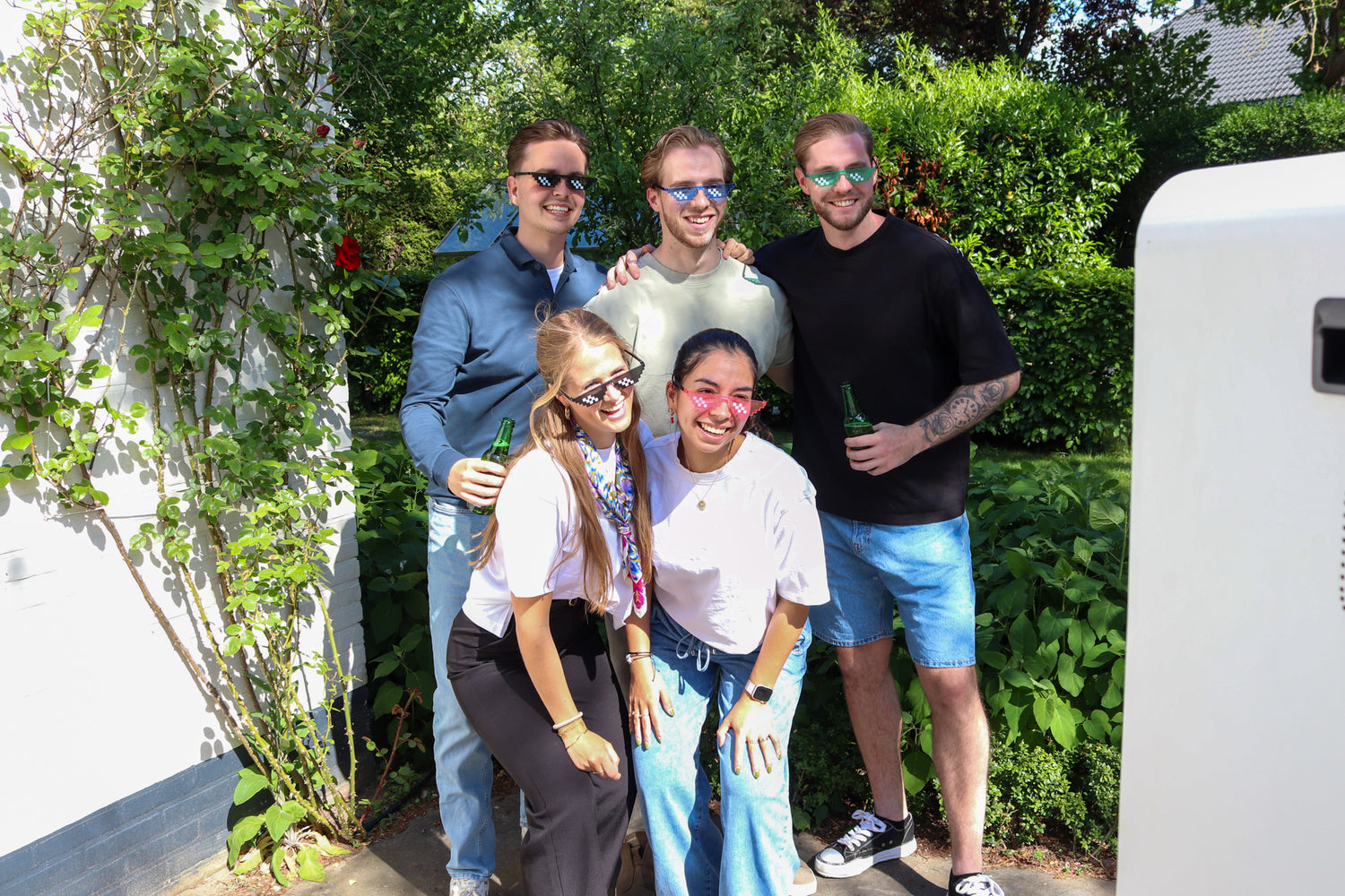 Groep feestgangers die vrolijk poseert voor de photobooth met feestelijke props zoals brillen, hoedjes en bordjes, lachend en in een feestelijke sfeer.